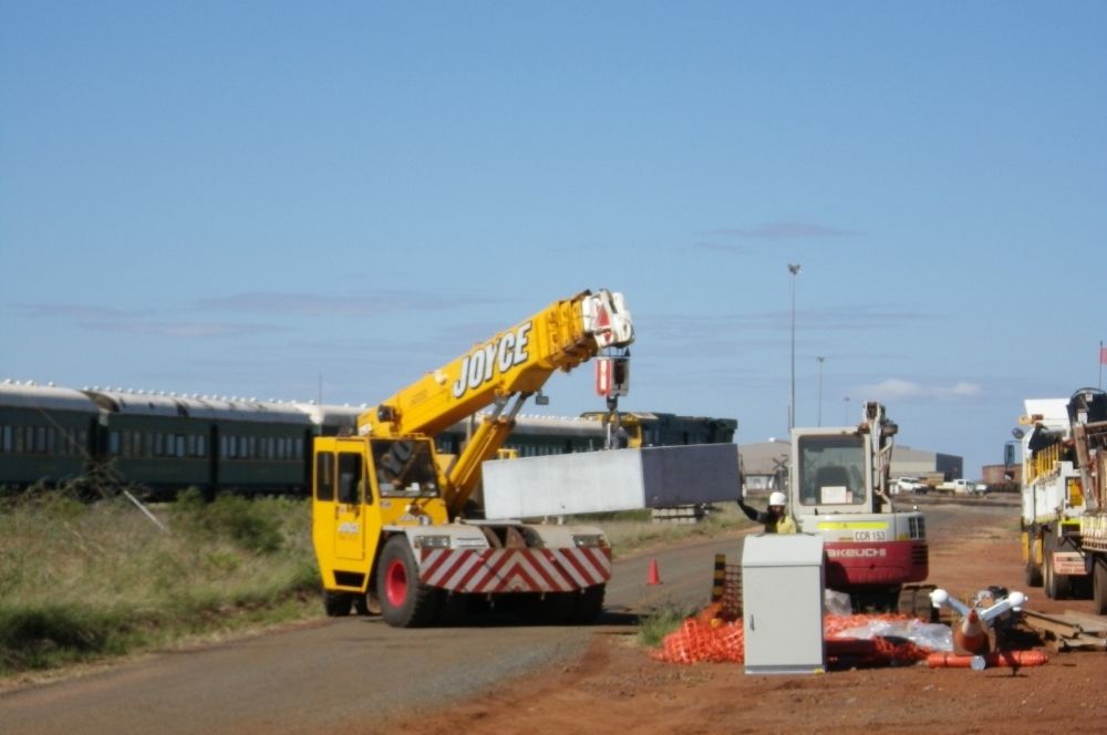 Our Guide to Concrete Footings: Depth, Concrete Volume and Curing Time 1 Mobile crane lifting a precast concrete pole base at an industrial worksite.